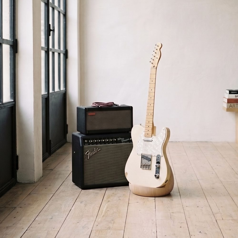 Telecaster crème sur la Stèle en bois clair, à côté d'un ampli